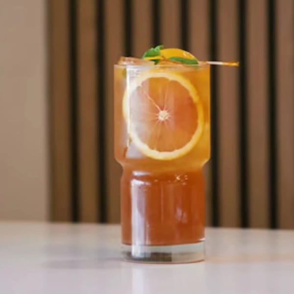 A tall glass of iced tea with an orange slice and mint garnish on a white table.