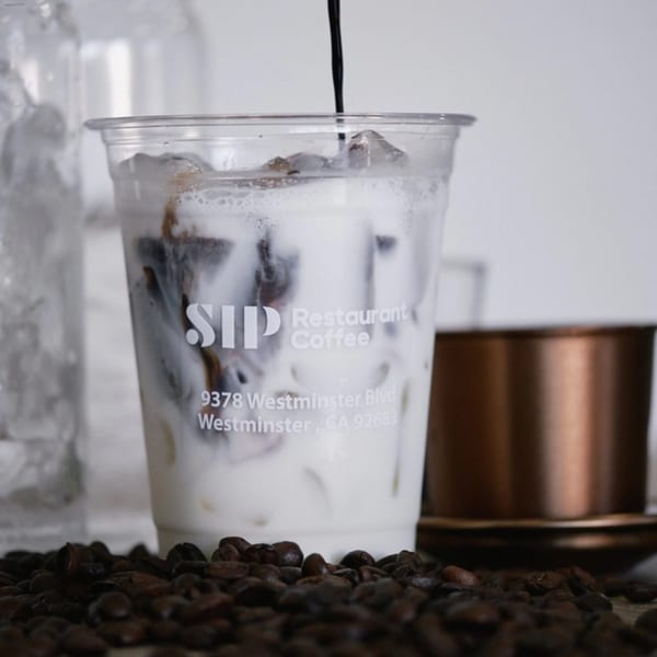 Iced Vietnamese coffee with milk being poured into a clear cup, surrounded by coffee beans.
