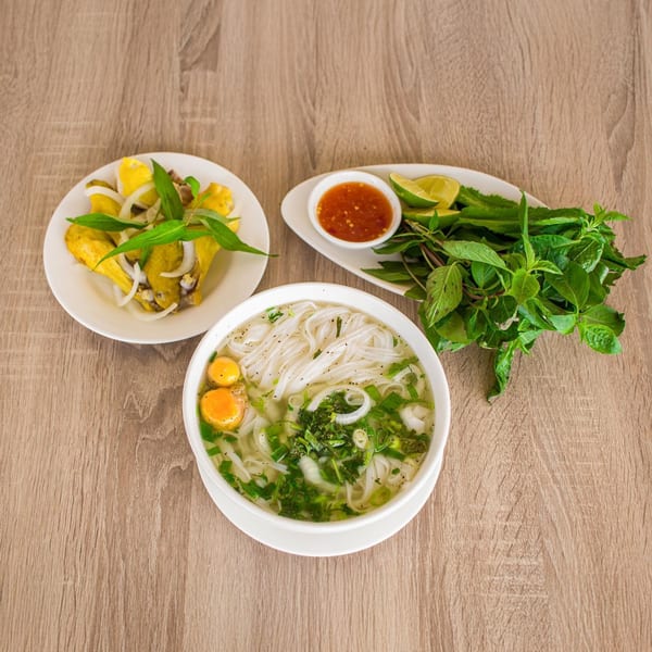 Vietnamese pho with quail eggs, a side of chicken, and fresh herbs with dipping sauce.