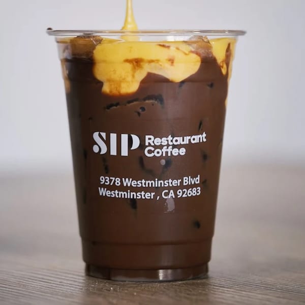 Iced coffee with a golden foam topping, branded "Sip Restaurant Coffee" on a wooden surface.