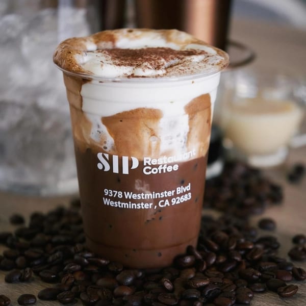 Vietnamese iced coffee with a creamy foam topping and cocoa powder, surrounded by coffee beans.