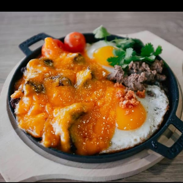 Vietnamese sizzling plate with eggs, ground meat, tomatoes, and a rich orange sauce.