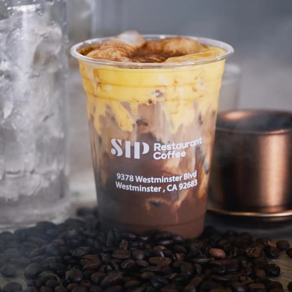 Iced Vietnamese coffee with creamy foam and cinnamon, surrounded by coffee beans.