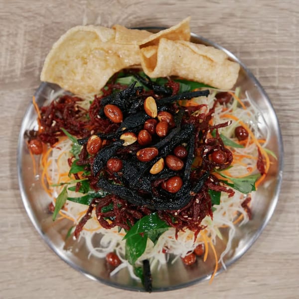 Vietnamese salad with shredded vegetables, dark crispy toppings, peanuts, and two large crackers.