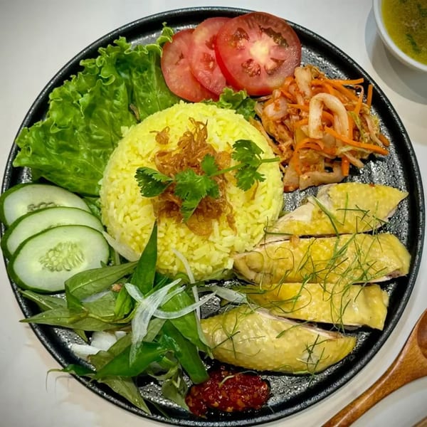 Vietnamese chicken rice with yellow rice, sliced chicken, fresh vegetables, and chili sauce.